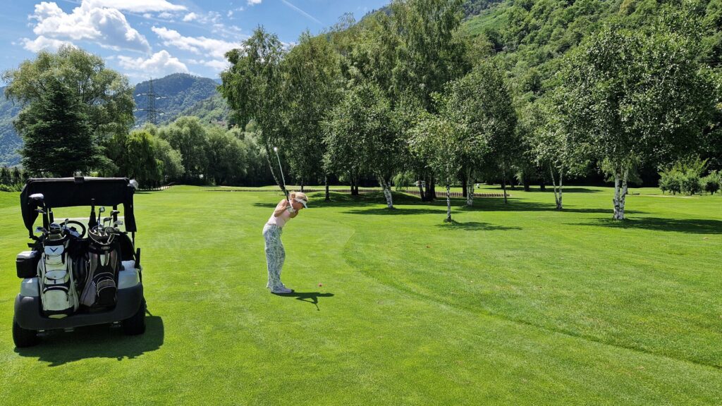 Golferin beim Schlag auf dem Golfplatz Lana neben einem Golfcart 